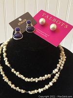 Full display of three jewelry items: two pairs of earrings on their original backing cards, and a multi-strand pearl-style necklace on black display.