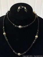 Full view of black beaded necklace with silver beads alongside matching clip-on earrings on black velvet display.