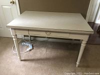 Full front view of the white wooden craft table showing the tabletop, drawer, legs, and power strip underneath.