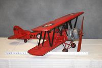 Angled front view of the red biplane model highlighting wing span and overall length with ruler for scale.