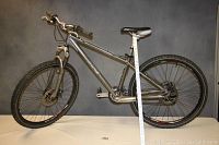 Side view of entire silver aluminum frame mountain bike showing gears, saddle, and handlebar setup
