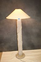 Full view of the decorative pillar-style floor lamp with leaf carvings and white large fabric shade, lamp turned on.