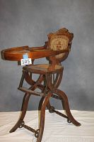 Full view of antique oak high chair showing foldable wheeled base, wooden frame, curved armrest, and tray surface.