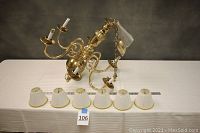 Full view of chandelier laid out on table with six detached white pleated shades and a ruler for scale