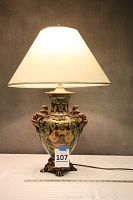 Full front view of lit table lamp showing urn shape, dragon handles, decorative feet and cream shade
