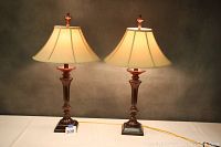 Pair of translucent brown table lamps side by side on a white surface with beige fabric shades and decorative finials.