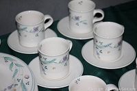 Close up of four porcelain cups and saucers showing the multicolored floral design with green leaves on white background.