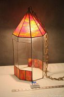 The planter shown from an angle highlighting orange stained glass dome and base with clear glass panels in between and the brass hanging chain.