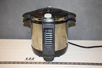 Front view of pressure cooker showing control panel and pull-out handles on a gray background with ruler.