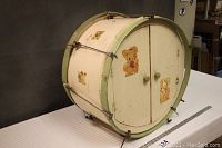 Side angle showing the circular shape of the wooden dresser, painted white with green trim and metal hardware resembling drum bands and lugs. Two doors with animal decals visible.