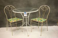 Front view of garden set showing round glass top table and two wrought iron chairs with patterned cushions.