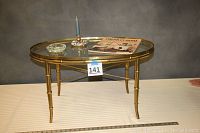 Front view of oval brass and glass coffee table with accessories on top