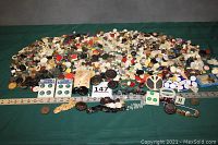 Wide view of a large pile of assorted buttons of various colors and sizes spread on a green cloth with a measuring tape beside them.
