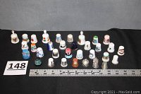Wide view of 32 assorted thimbles arranged in rows on black background with measuring ruler and item number card.