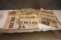 Full view of assorted WWII-era newspapers laid out on table, showing their aged condition and large historic headlines.