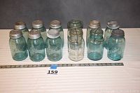 Overall overview of the dozen Ball canning jars showing 11 blue jars and one clear jar in multiple rows and including a measuring tape for scale.