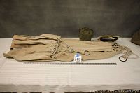 Canvas hammock folded with metal rings and cords visible, placed on a white surface with a measuring ruler.