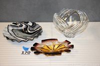 Three glass pieces: purple-yellow dish, black-white slag plate, and clear Lenox bowl arranged on striped cloth