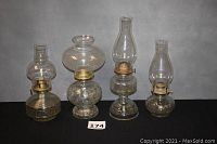 Four vintage kerosene oil lamps arranged in a row showing their full height and glass chimneys.