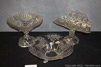 Three antique glass serving pieces photographed together on black fabric background showcasing their size and design.