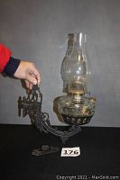 Full view of cast iron oil lamp bracket with clear glass oil lamp fitted, showing swivel mechanism and overall condition.