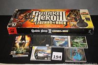 Guitar Hero III Legends of Rock box with wireless guitar controller box and several video game cases beneath it showing various titles