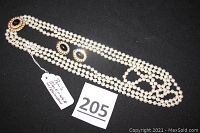 Full view of the three-strand pearl necklace with black stone clasp and matching earrings on black background.