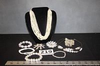 Full lot showing 8-strand pearl necklace on black bust, six bracelets in front, and two floral pins center front