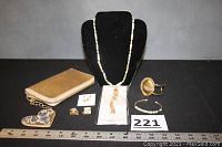 Gold Talbots clutch purse, Chico's necklace on black display, vintage pierced earrings, clip earrings, ceramic bead necklace, two bracelets displayed with measuring tape for scale and lot number 221.