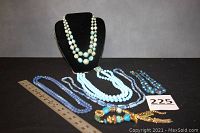 Photo of the single black velvet display bust holding the multi-strand light blue necklace with spherical beads and gold accents, with five other blue jewelry pieces laid out next to a ruler and a lot number card.