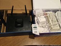 Box containing a black Linksys AC2200 Tri-band Mesh WiFi router with four antennas and five white Velop Tri-band AC4400 mesh units with cables arranged inside.