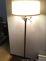 Full view of the floor lamp lit, showing shade, multiple bulbs, pole and some surrounding room context.