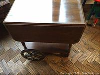 Side angle showing large black spoked wheels, expandable side, and lower shelf.