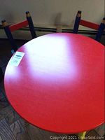 Top view of round red kids table showing table top and part of two pencil motif chairs behind.