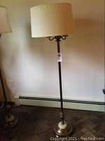 Full view of the vintage floor lamp with a round beige fabric shade placed on a dark brass pole and a round marble base.