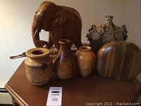 Photo showing carved wood elephant figurine, four varied vases, and woven basket arranged on wooden furniture.