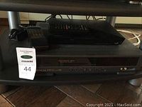 View of Sony Blu-ray/DVD player and Hitachi VHS video deck stacked with remotes on top