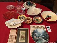 Overview of assorted vintage serve plates, dishes, crystal bowls, and framed items on a red tablecloth.