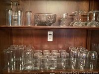 Wood cabinet shelf with assorted tall cylindrical tumblers, mid-size glasses and one cut crystal bowl