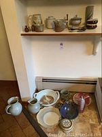 Assorted pottery displayed on shelf and floor including pitchers, bowls, mugs, jar, plates