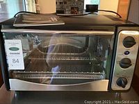 Front view of Paderno toaster oven with glass door, wire rack inside, and manual on top