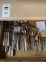 Top-view photo showing stainless steel forks, knives, and spoons laid out in a cardboard box.