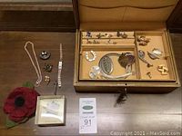 Full lot displayed on wood surface in open tan jewelry box and loose on table