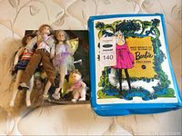 All dolls and the blue plastic Barbie doll case on mattress