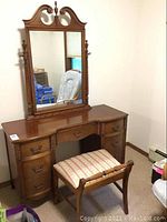 Full view of antique wooden vanity with attached mirror and matching upholstered stool beneath it. Shows overall condition and details.