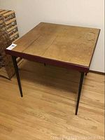 Card table angled view showing water stains and fold lines on wood top with metal legs.
