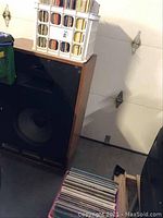 Plastic milk crate filled with vinyl record sleeves atop a wooden speaker cabinet showing crate and record thickness