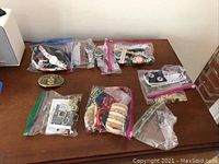 Overview photo showing multiple bags containing wristwatches, belt buckle, and assorted costume jewelry on a wooden surface.