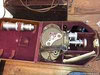 Open fitted leather carrying case with camera body in maroon fabric compartment, two additional lenses on left, instruction manual