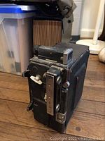 Side view showing textured black leatherette body and chrome hardware with visible wear and soiling on the vintage Speed Graphic camera.